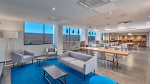 A spacious hotel lobby with a large seating area, a kitchen in the background, and large windows offering a view of the desert landscape. - City Express by Marriott Hermosillo Expo (Hermosillo)