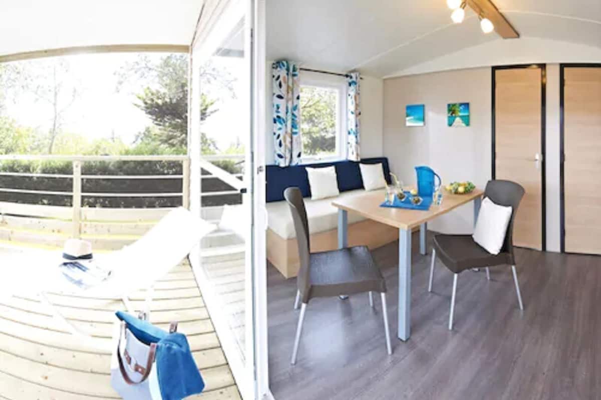 A modern room with a wooden deck, a sofa, a dining table with chairs, and a view of greenery outside.