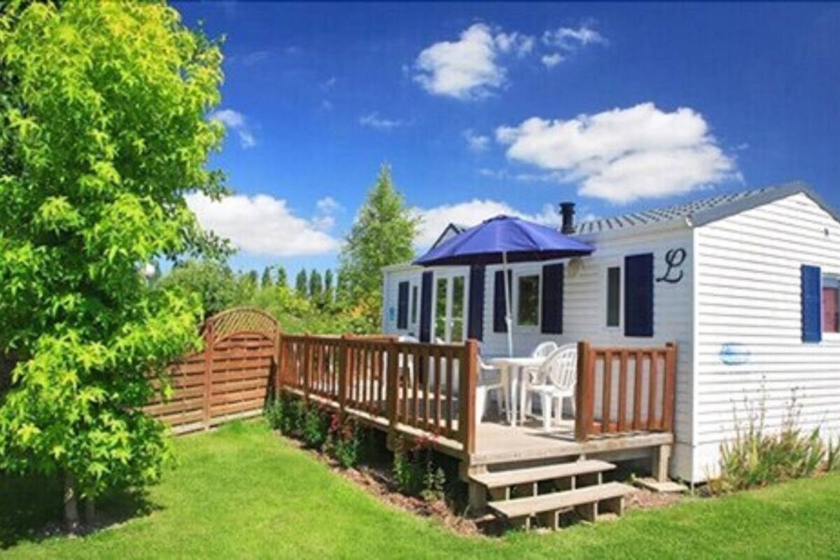 A small, single-story cabin with a porch, a covered outdoor seating area, and a fenced yard.