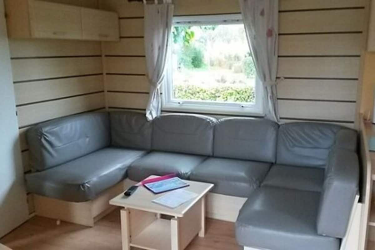 A compact living space with a grey sofa, a small table with papers, and a window with curtains.