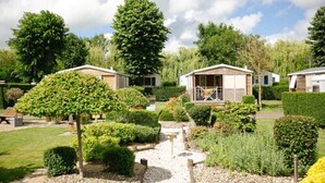 A row of single-story mobile homes with a garden pathway leading to a central area with a bench and a small fountain. - Camping Haliotis (Pontorson)