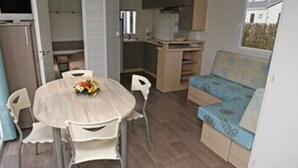 A compact living space with a round dining table, a sofa, and a kitchenette area. - Camping Haliotis (Pontorson)