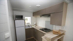 A compact kitchen with a refrigerator, microwave, stove, and sink. - Camping Haliotis (Pontorson)