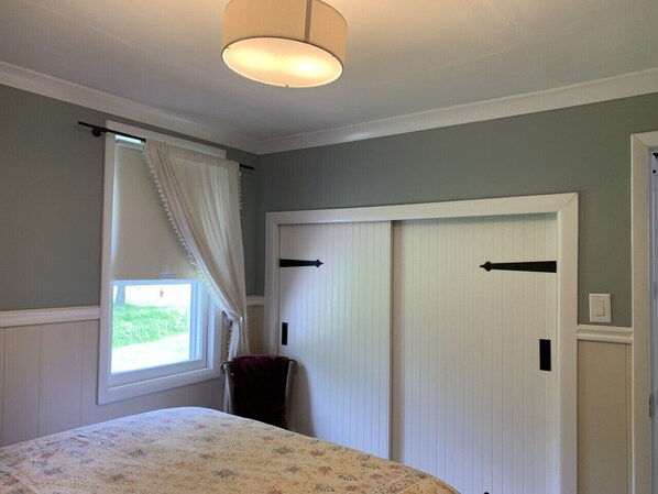 A bedroom with a bed, a window with curtains, a chair, and two closets.