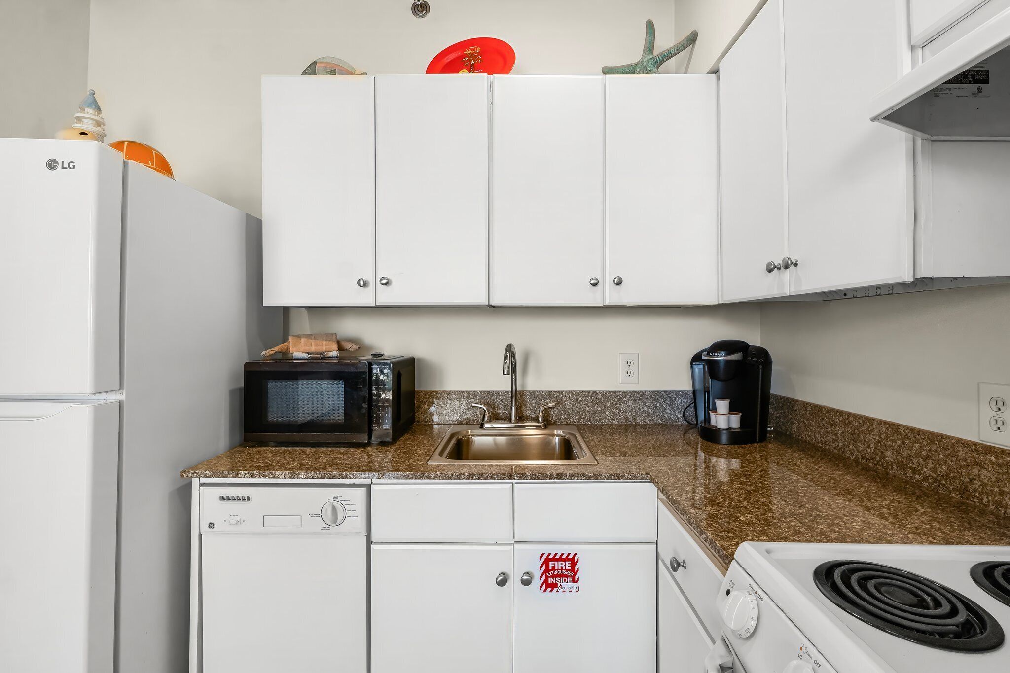A compact kitchen with white cabinets, a microwave, a coffee maker, and a dishwasher.