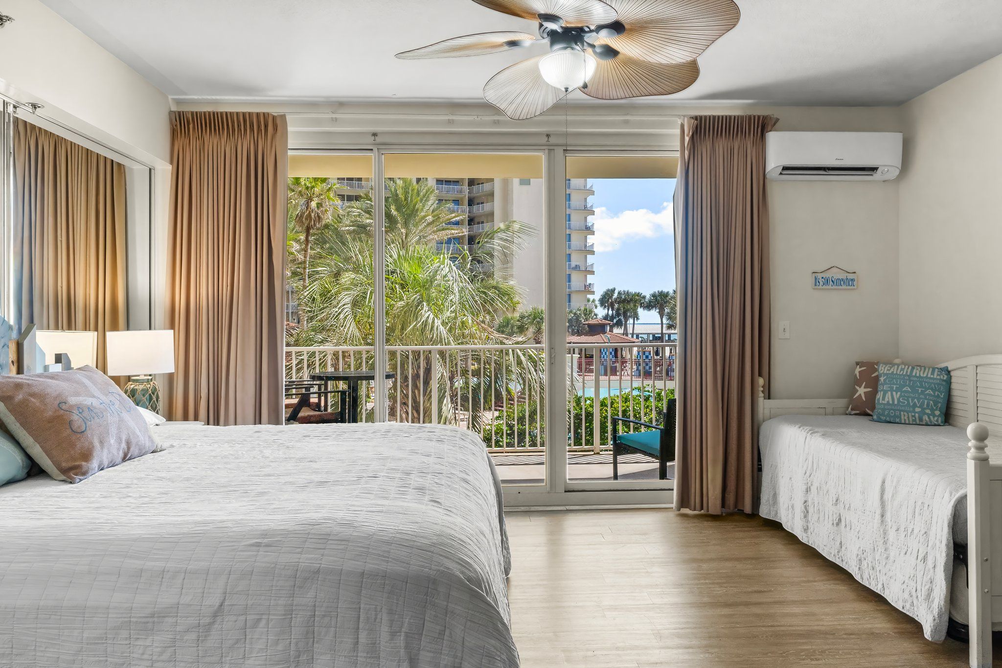 A hotel room with a balcony, a bed, a desk, and an air conditioning unit.