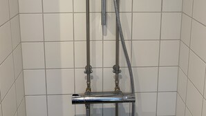 A shower with a handheld showerhead and a fixed overhead showerhead, both mounted on a wall with a grid of square tiles. - Apartment 1 bedroom Grønnegade (Copenhagen)