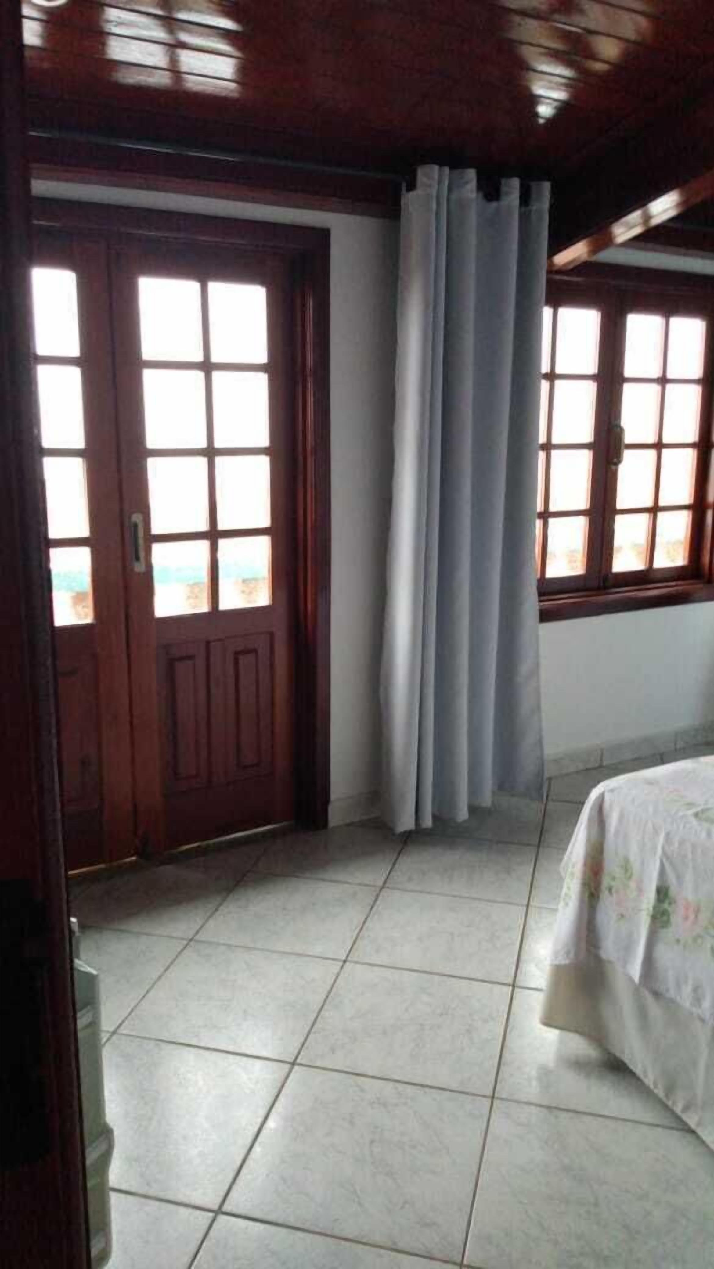 Um quarto com porta de madeira, janela com cortina e cama com colcha florida.