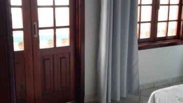 Um quarto com porta de madeira, janela com cortina e cama com colcha florida.