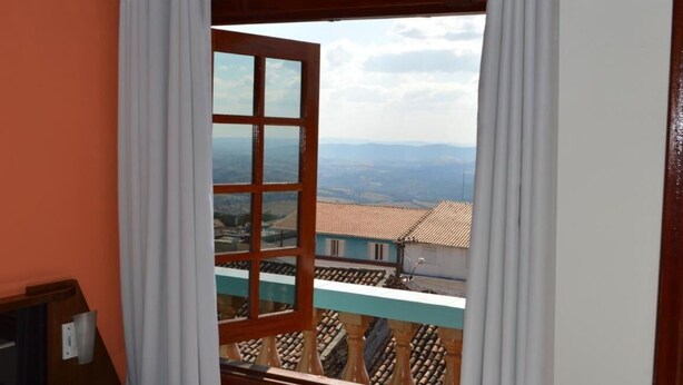 A room with a view of a tiled roof and distant landscape. - Pousada Souza Reis (Sao Thome das Letras)