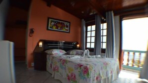 A bedroom with a bed, a nightstand, a painting on the wall, and a window with curtains. - Pousada Souza Reis (Sao Thome das Letras)