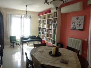 A dining area with a table set for two, a bookshelf, and a radiator on the wall.