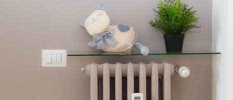 A radiator with a thermostat, a power outlet, and a shelf with a plush toy and a potted plant.