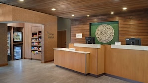 A reception area with a wooden reception desk, a refrigerator stocked with beverages, and a wall-mounted decorative piece. - Fairfield Inn & Suites by Marriott Locust Grove I-75 South (Locust Grove)