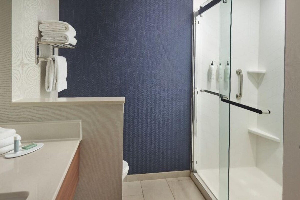 A bathroom with a glass shower enclosure, a white sink with a towel rack, and a dark patterned wall.
