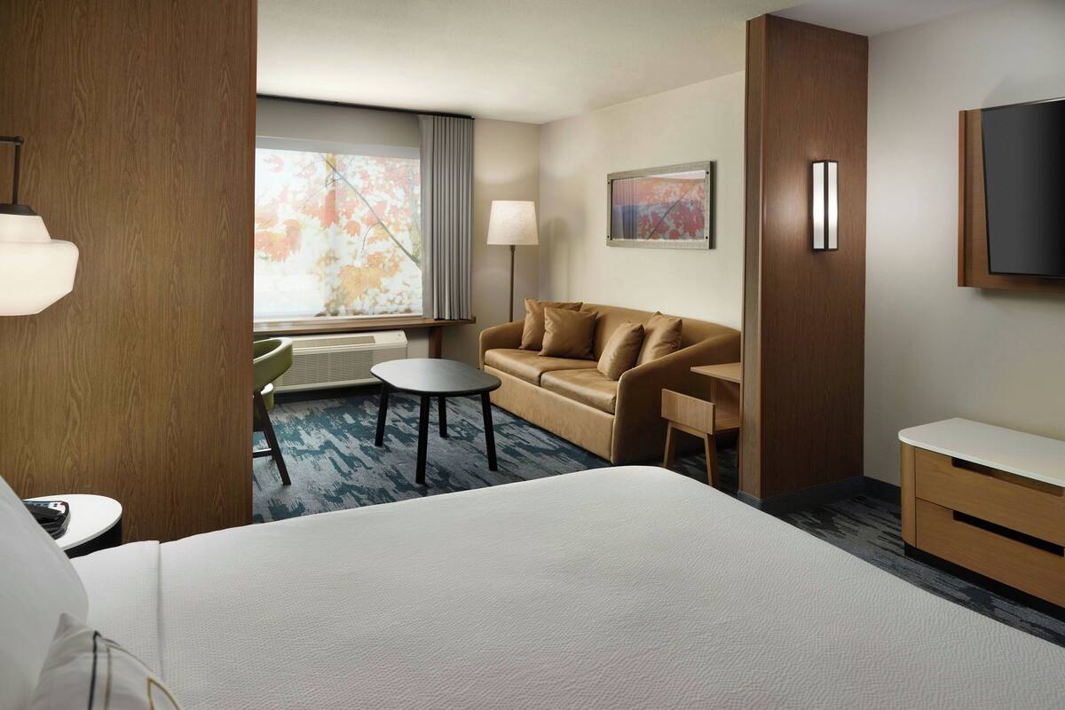 A hotel room with a large bed, a sofa, a small table, a desk, a TV, and a window with curtains.