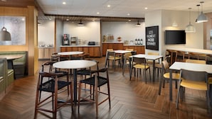 A modern cafe with wooden flooring, round tables, and chairs. There is a counter with a coffee machine and a chalkboard with motivational writing. - Fairfield Inn & Suites by Marriott Locust Grove I-75 South (Locust Grove)