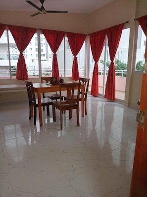 A dining area with a table and chairs, large windows with red curtains, and a ceiling fan. - Hotel Boutique Bahia Plaza (Santa Marta)