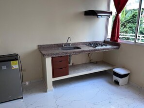 A compact kitchen with a granite countertop, a built-in sink, a gas stove, a small refrigerator, and a trash bin. - Hotel Boutique Bahia Plaza (Santa Marta)