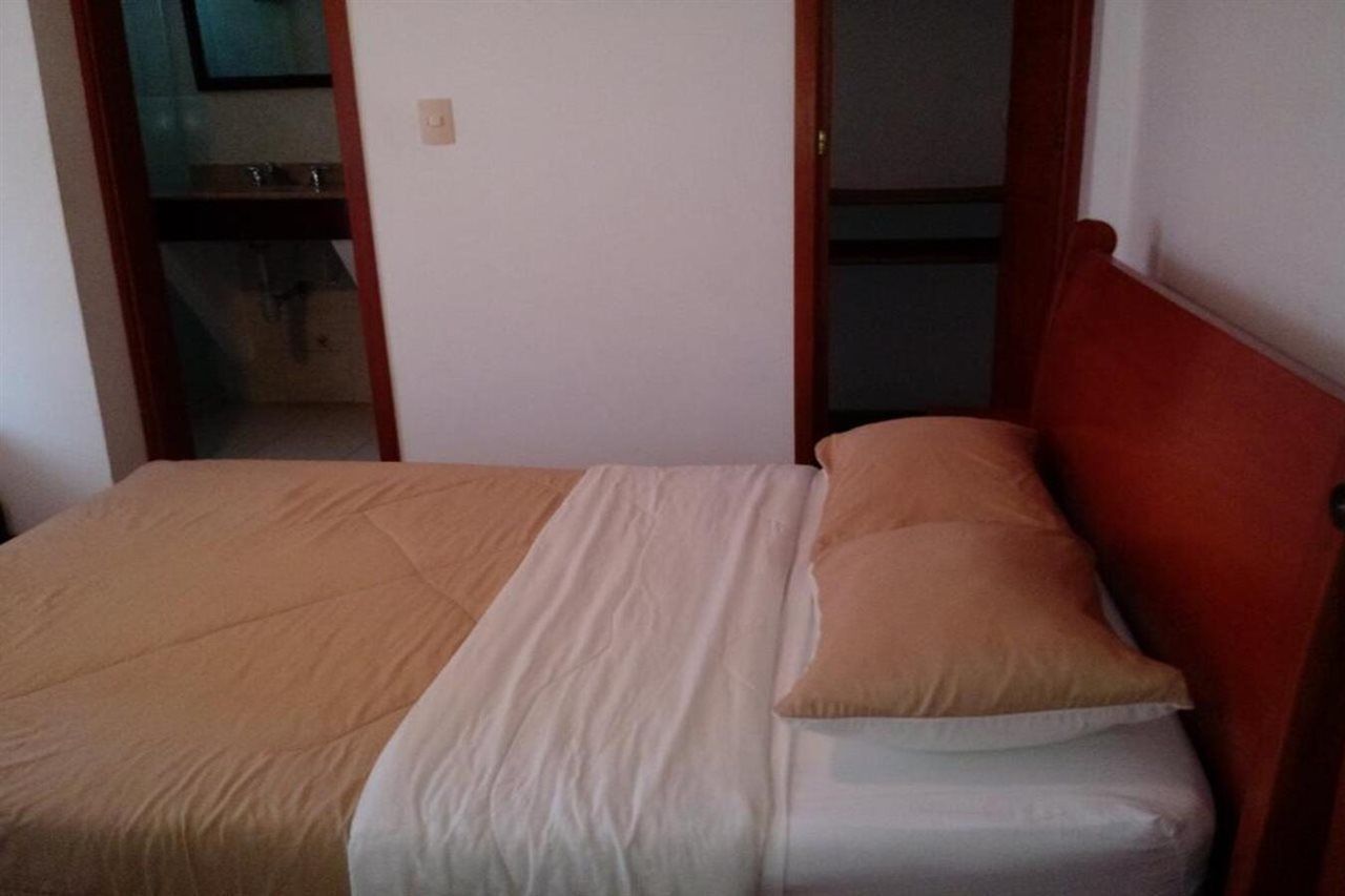 A single bed with a wooden headboard, a beige and white bedspread, and a single beige pillow.