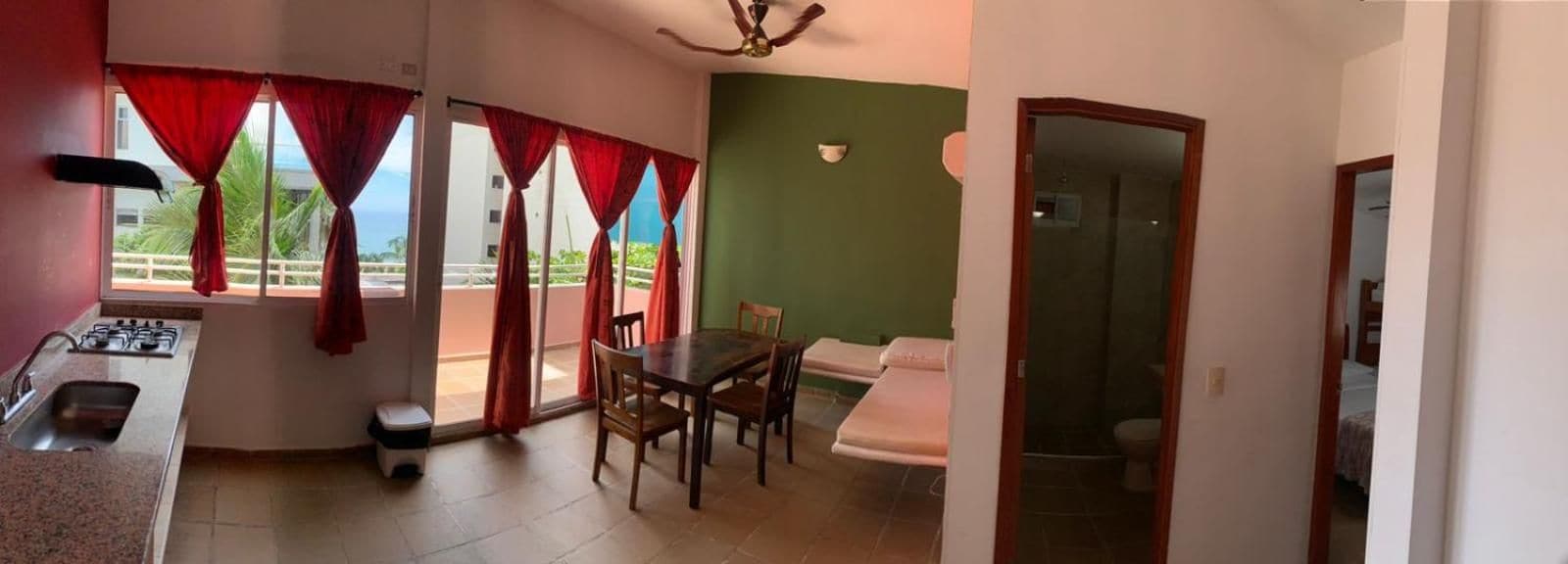 A room with a kitchenette, a dining area with a table and chairs, a sofa, and a view through the window.