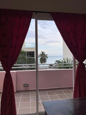 Un balcó amb vista al mar, una palmera i un edifici al fons.