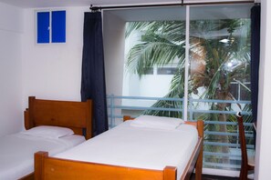 A room with two wooden beds, a blue curtain, and a view of palm trees through a glass door. - Hotel Boutique Bahia Plaza (Santa Marta)