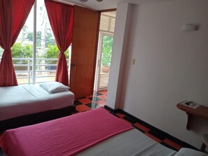 A hotel room with two beds, a window with red curtains, a door leading to an outdoor area, and a check-in counter.