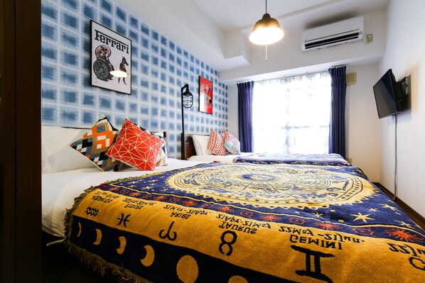 A neatly made bed with a patterned bedspread, a wall-mounted air conditioner, and a window with curtains. - Grand Court Namba 402 (Osaka)