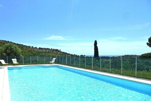 Ein rechteckiger Swimmingpool mit klarem, blauem Wasser, umgeben von einem grünen Zaun. Weiße Liegestühle befinden sich am Poolrand.