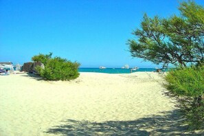 A beach with clear blue water, a few boats, and some greenery.