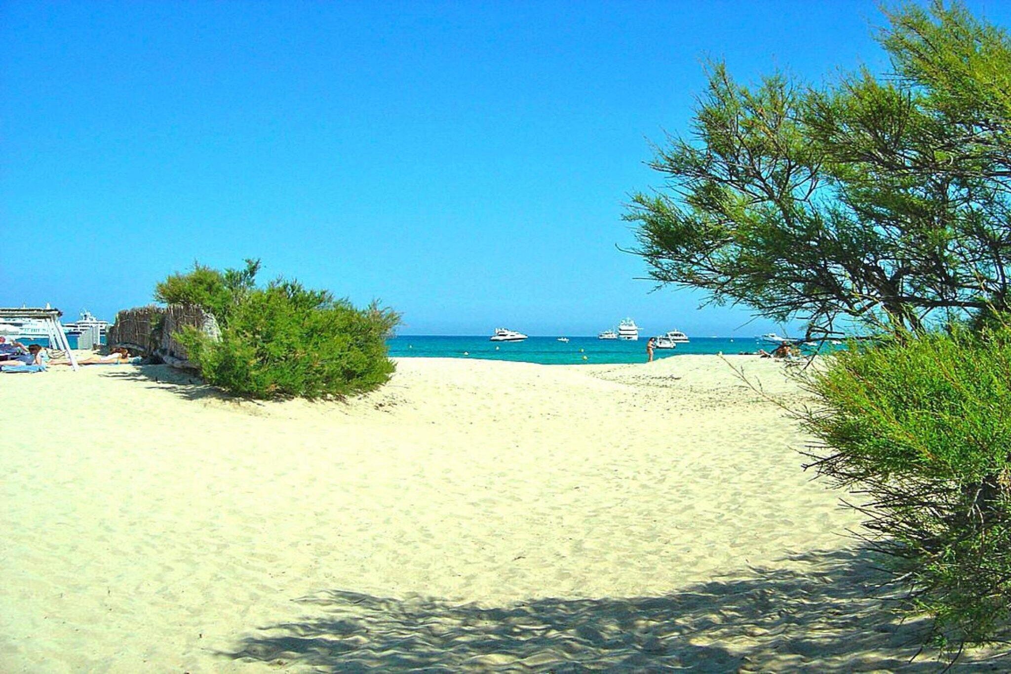 A beach with clear blue water, boats, and a few people.