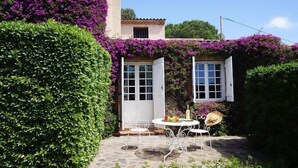 A patio with a table and chairs, surrounded by lush greenery and purple flowers. - Villa in Roquebrune with Sea View & Pool (Roquebrune-sur-Argens)