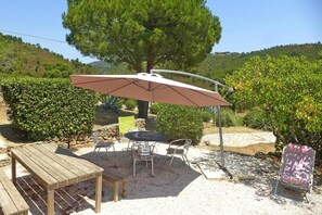 Eine Terrasse im Freien mit Tisch, Stühlen, einem großen Sonnenschirm und einem Baum.