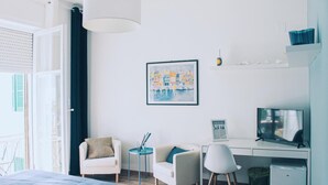 Habitación de hotel moderna con una cama, dos sillones, un escritorio con computadora, televisor y un refrigerador pequeño.