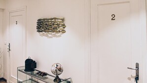 Un pasillo con dos puertas, una con el número 3 y la otra con el 2. Hay una mesa de vidrio con un globo terráqueo y un bolso negro encima, además de una decoración de peces en la pared.