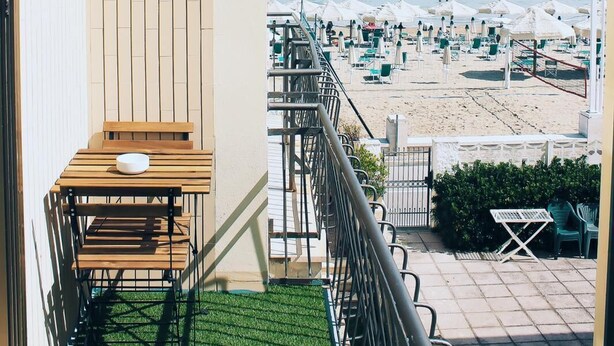 Un balcón con vista a la playa, una mesa de madera y una pequeña zona ajardinada.