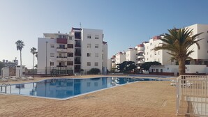 Ein Schwimmbecken mit gefliestem Sonnendeck, umgeben von Wohngebäuden mit Balkonen und Palmen.