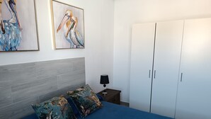 Ein Schlafzimmer mit einem Bett, zwei Kissen, einem Nachttisch mit Lampe, einem Kleiderschrank und zwei Bildern an der Wand.