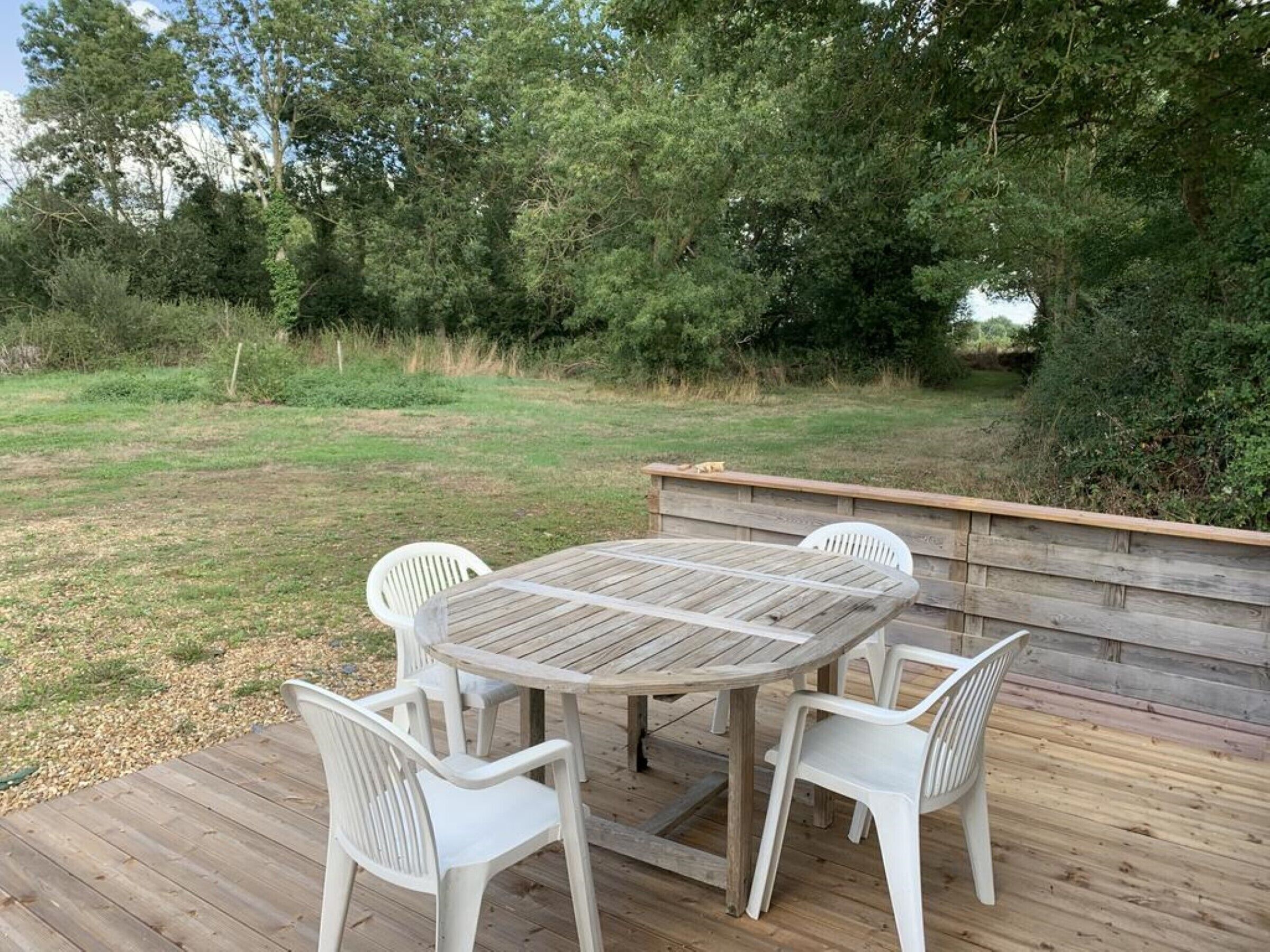 An outdoor wooden deck with a round table and four white plastic chairs.