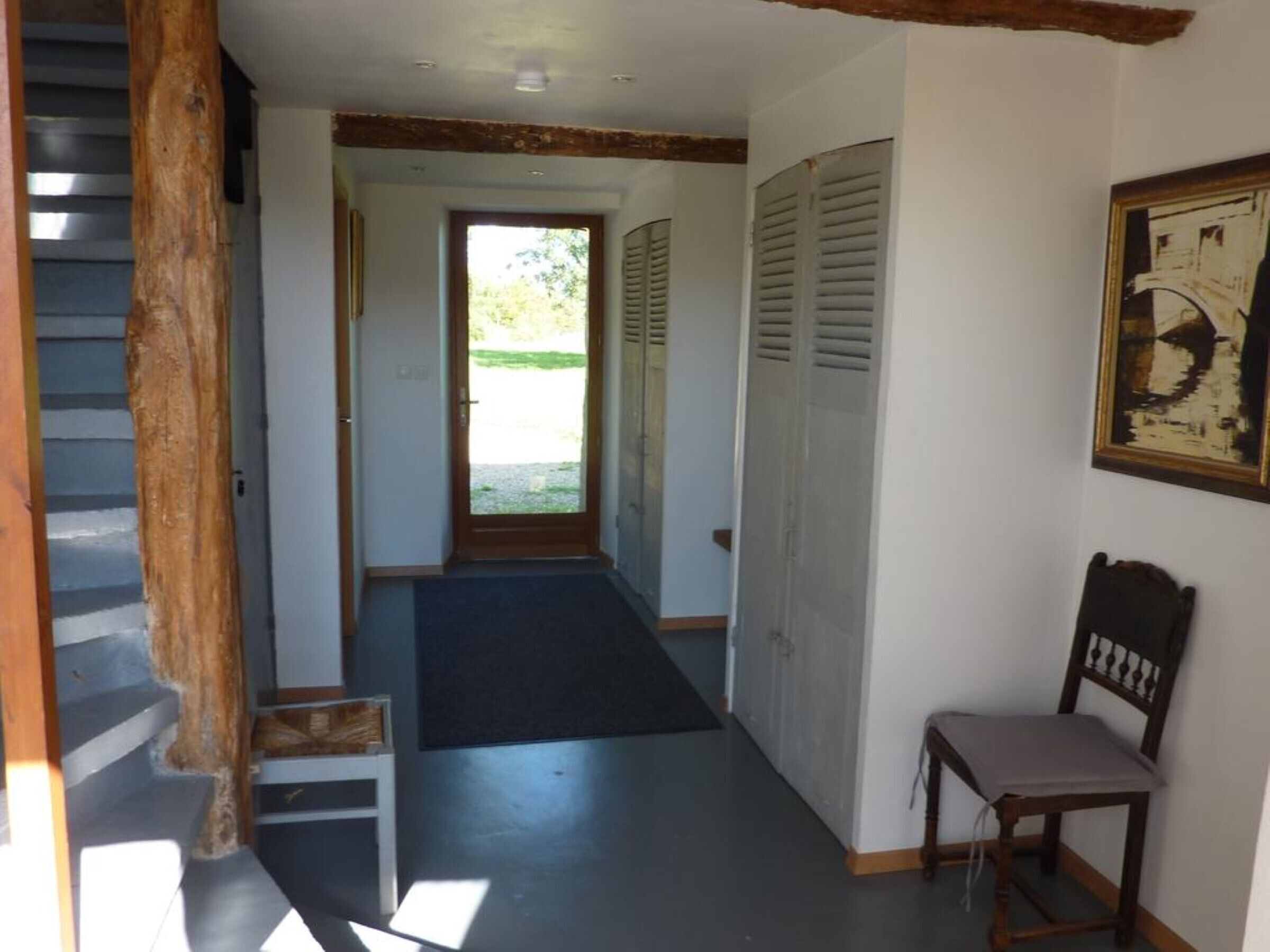 Un couloir étroit avec un escalier en bois sur la gauche, une porte au fond et une chaise sur la droite.