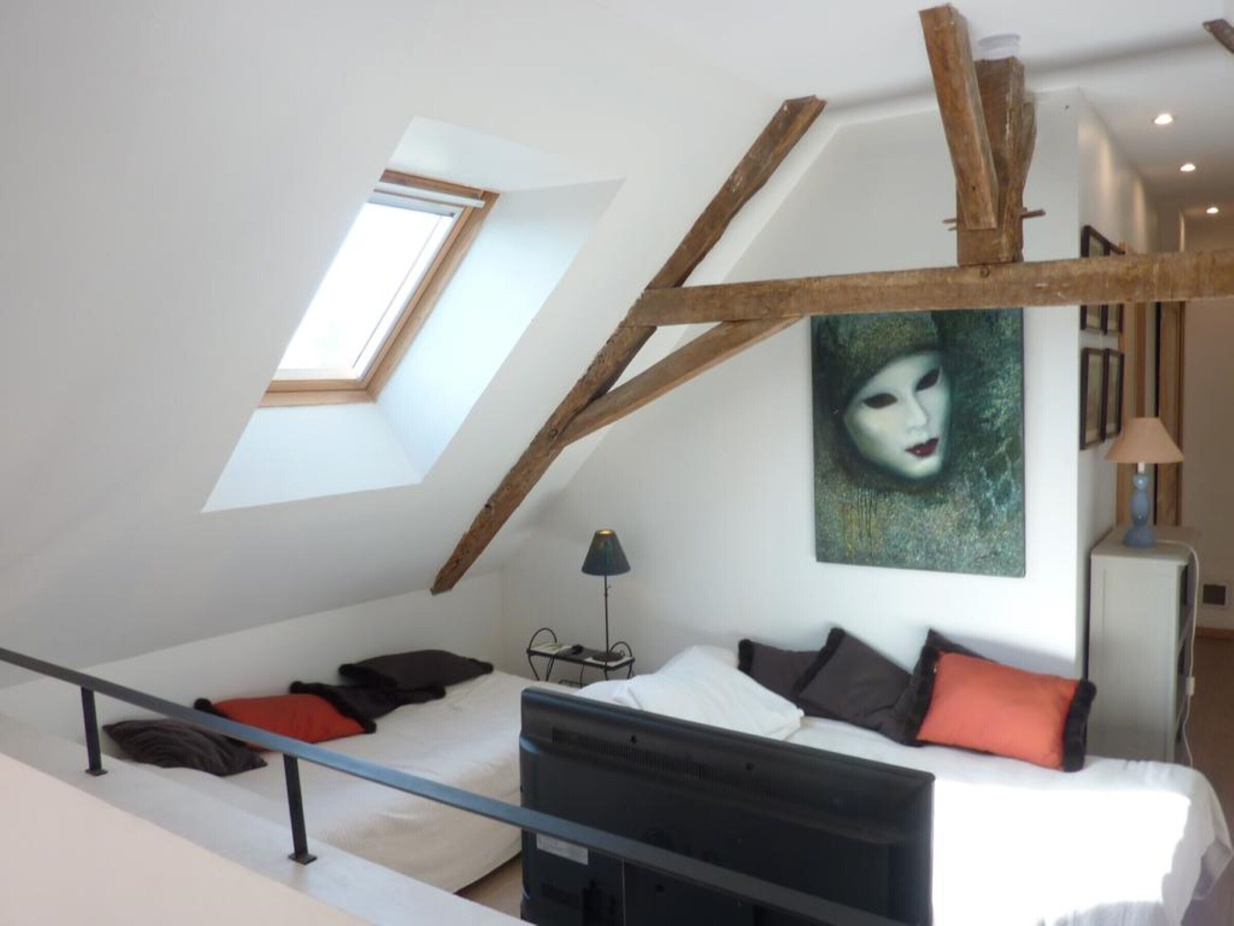 Une chambre de style loft moderne, avec un plafond en pente, un puits de lumière, un lit agrémenté de plusieurs coussins, un bureau et un tableau accroché au mur.