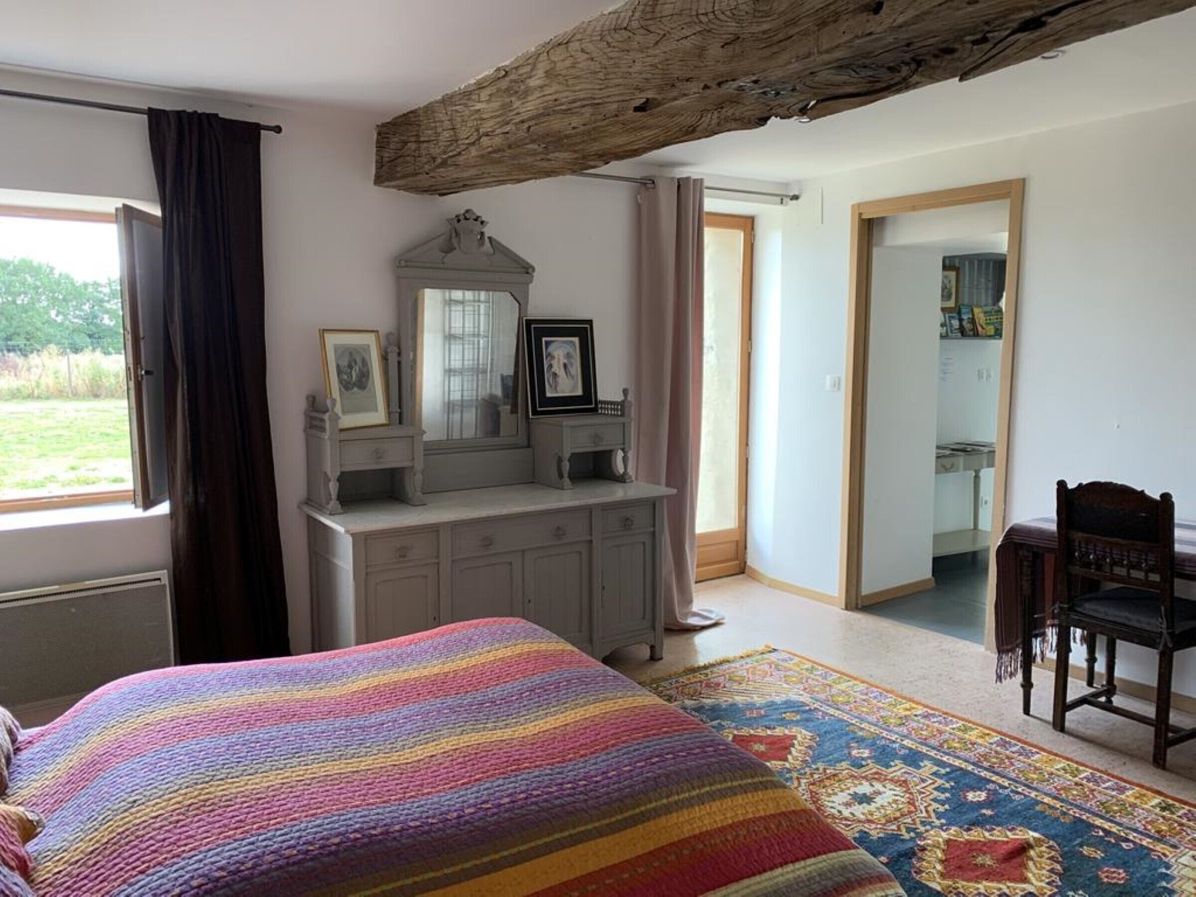 A bedroom with a bed, dresser, mirror, and a view of the outdoors.