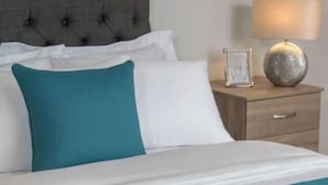 A neatly made bed with white and teal bedding, a tufted headboard, and a bedside table with a lamp and a picture frame.