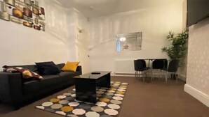 A modern living room with a black sofa, a coffee table, and a patterned rug. There is a dining area with a table and chairs.