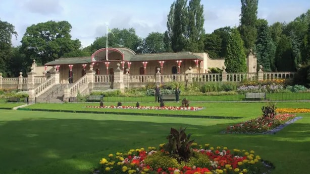 A historic building with a grand entrance, a well-maintained garden with colorful flower beds, and a clear sky.