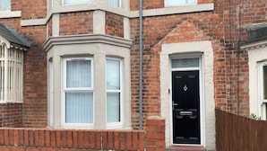 A corner house with a bay window, a black door with the number 25, and a brick wall.
