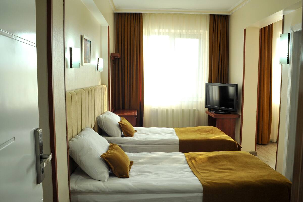 A hotel room with two beds, a television, and a window with curtains.