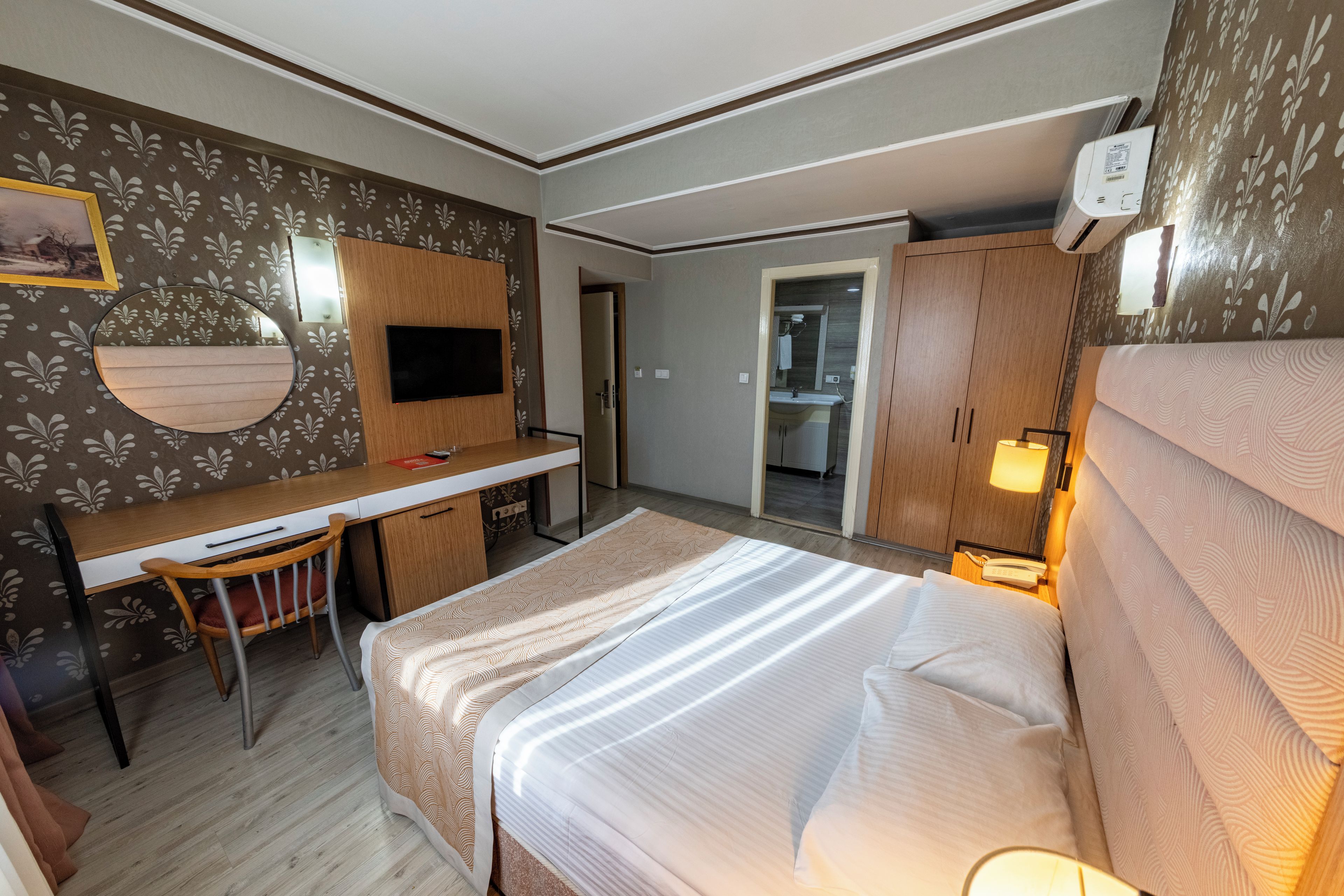 A hotel room with a bed, a desk, a chair, a television, and a wardrobe.