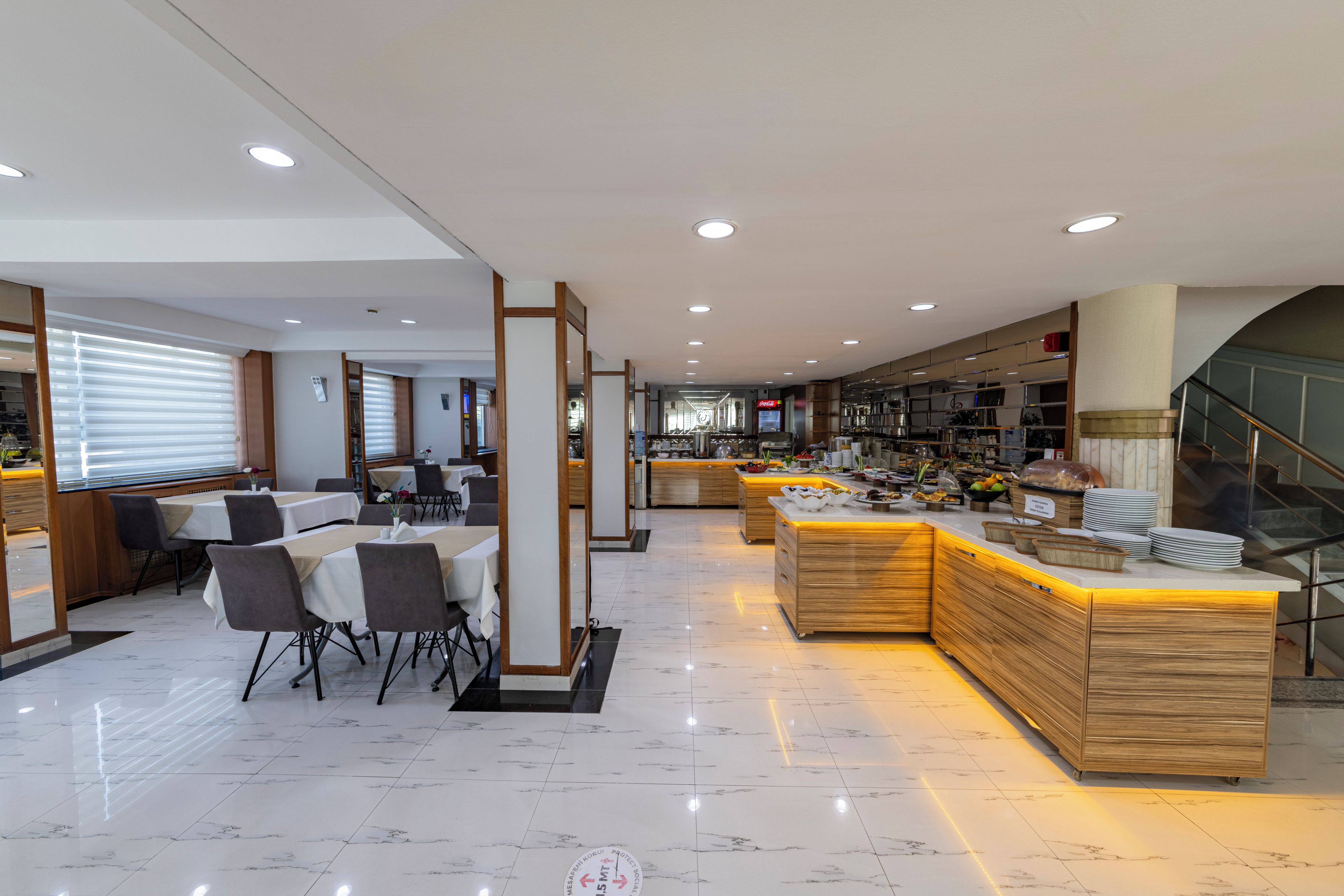 Un moderno hall de hotel con zona de comedor, mostrador de recepción y una escalera.